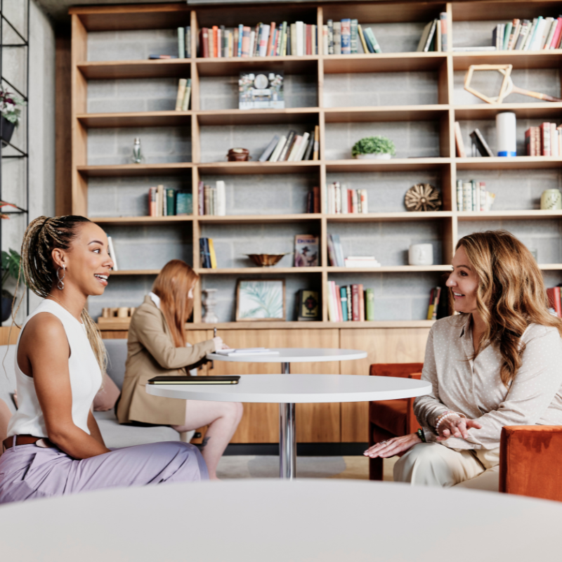 Two colleagues sit and chat at work.